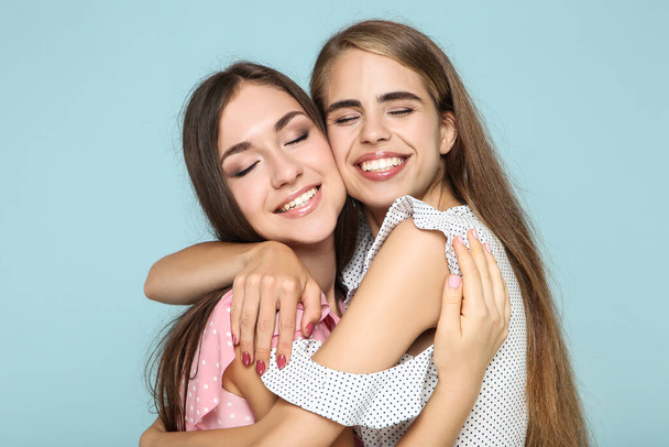 Young happy girlfriends in fashion dresses hugging each other on blue background - Fotografie, Obrázek