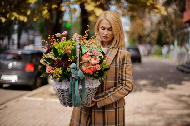 attractive woman holds wicker basket with various flowers and look at it - Foto, Bild