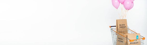 cultivo panorámico de bolsas de compras con letras de viernes negro en el carro con globos de color rosa sobre blanco - Foto, Imagen