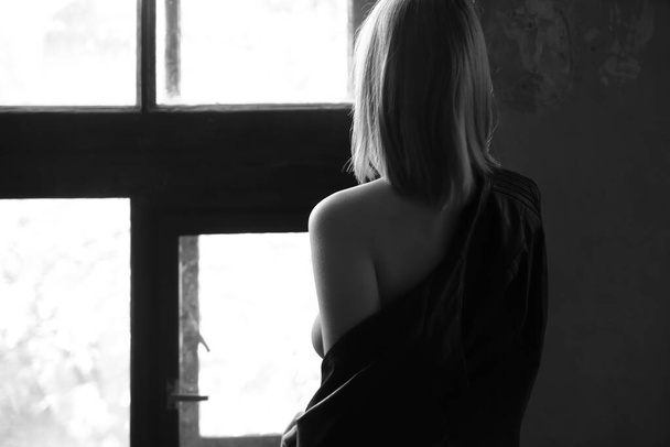 Achteraanzicht van een mooie eenzame vrouw in zwart leren jasje bij het raam. - Foto, afbeelding