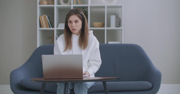 Egy fiatal nő fejhallgatós konferenciát visel, ami laptopbeszélgetésekre hív online tanárokat, tanulnak, otthonról dolgoznak. Női diák és tanulás segítségével számítógépes webkamera chat jegyzetel. Távolsági oktatás koncepciója - Felvétel, videó