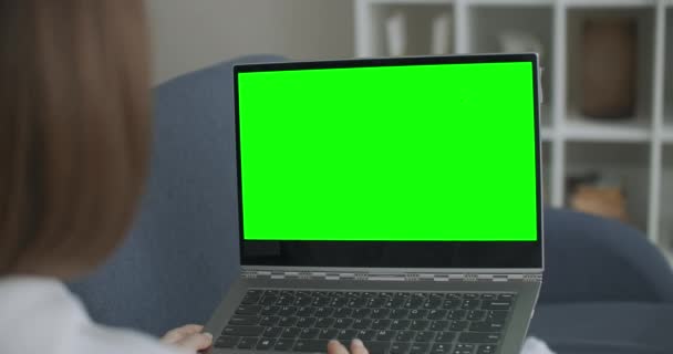 Woman at Home Sentado en un sofá funciona en una computadora portátil con pantalla falsa verde. El Coronavirus Covid-19 pone en cuarentena la educación remota o el concepto de trabajo. Chica usando la computadora, Navegando a través de - Imágenes, Vídeo