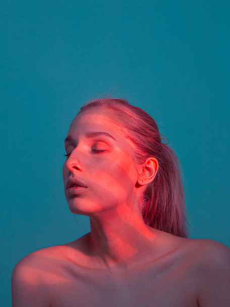 Studio portrait of young pretty girl with coral light on her face and naked shoulders - Foto, immagini