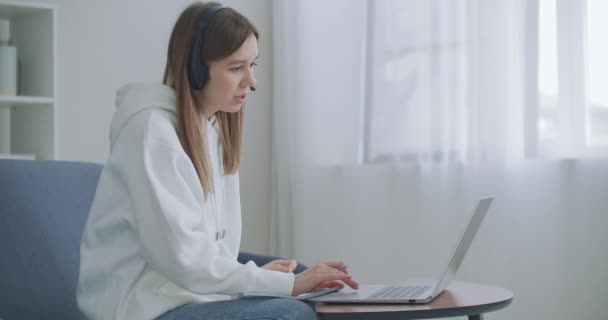 Młoda kobieta nosi słuchawki konferencji dzwoniąc na laptopy rozmowy z nauczycielem online studiuje, pracuje w domu. Lady student e-learning przy użyciu czatu internetowego komputera robi notatki. Koncepcja kształcenia na odległość - Materiał filmowy, wideo
