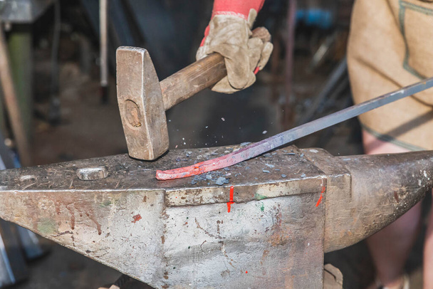 El herrero golpea la varilla roja caliente con un martillo y las piezas vuelan de la pieza de trabajo - Foto, imagen