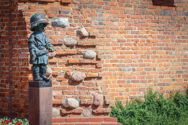 Памятник маленькому повстанцу в огромных немецких шлемах и сапогах, участнику Варшавского восстания 1944 года против красного кирпича средневековых городских стен - Фото, изображение