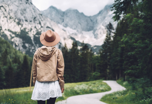 Beautiful young woman stands on road and looking at mountains. Hiker girl enjoys view on Alps and beauty of wild nature outdoors. Adventure travel in Slovenia, Europe. Freedom Natural Lifestyle - Valokuva, kuva