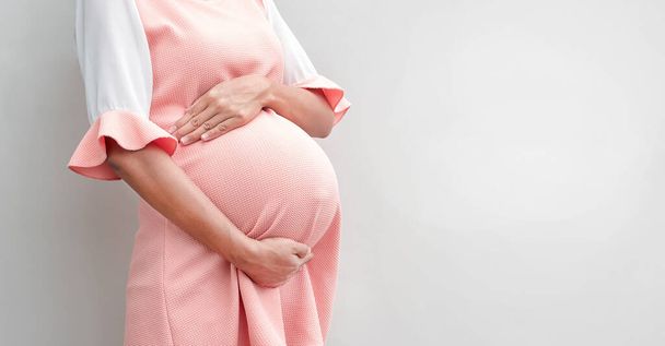 Беременная женщина в платье держит руки на животе на белом фоне, копирует пространство - Фото, изображение