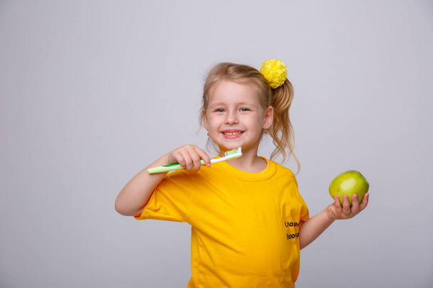 Pieni tyttö hammasharjan kanssa. Pieni tyttö hammasharjan ja omenan kanssa. Päivittäisen hygienian käsite. Eristetty valkoisella pohjalla - Valokuva, kuva