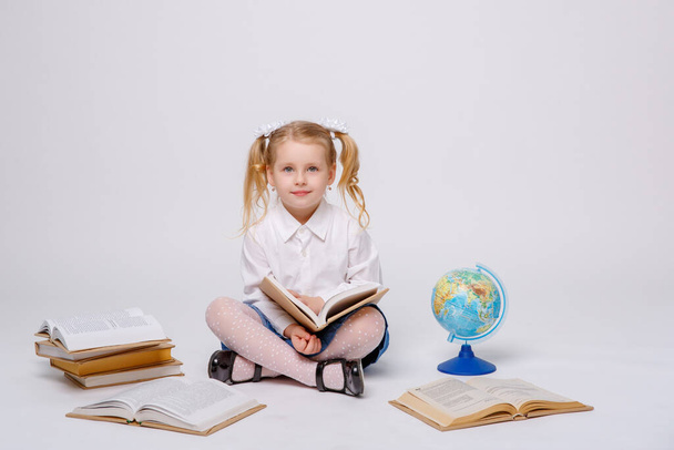 Okul üniformalı küçük bir kız beyaz bir arkaplanda kitap okuyor. - Fotoğraf, Görsel