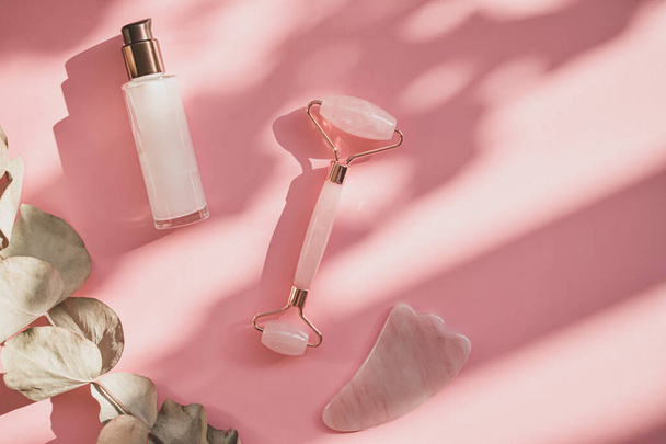 Massage with a quartz roller for the face with pink natural jade. Gouache massage tool, with beauty serum oil. Anti-aging and lifting at home. Facial care massage and relaxation concept. - Photo, Image