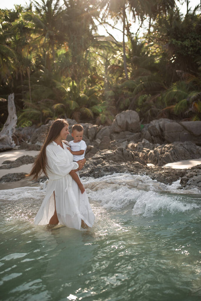 Äiti kävelee taivaansinisellä merellä ja kantaa poikaa sylissään - Valokuva, kuva