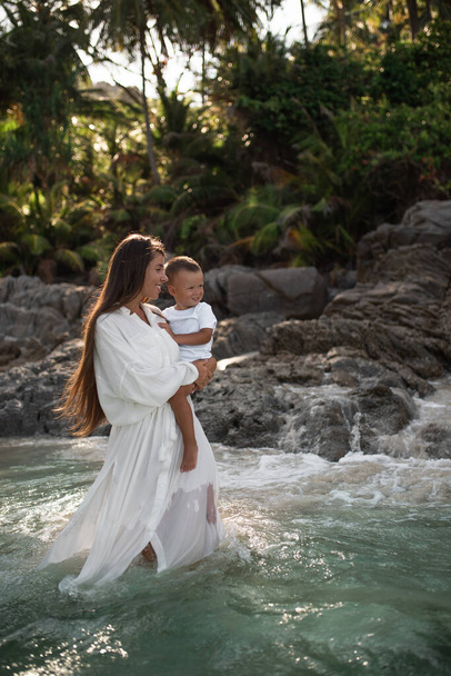 Äiti kävelee taivaansinisellä merellä ja kantaa poikaa sylissään - Valokuva, kuva