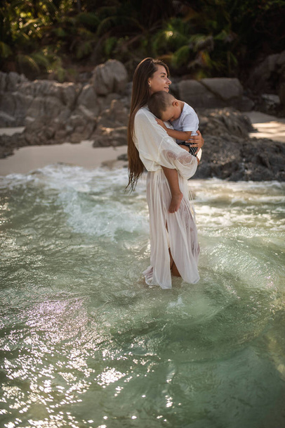 Matka spaceruje po lazurowym morzu i nosi syna w ramionach - Zdjęcie, obraz
