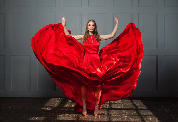 Mujer feliz en soplado vestido sedoso rojo posando en el interior - Foto, Imagen