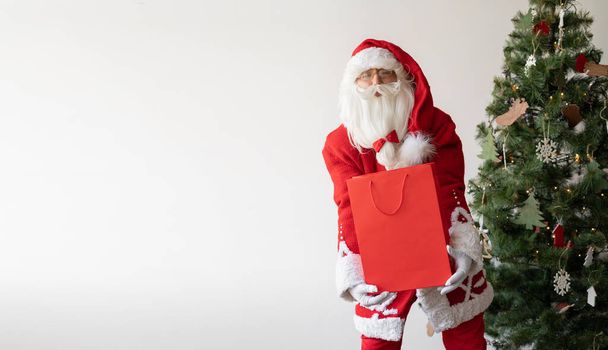サンタクロースは大きな買い物袋を持ってクリスマスツリーの近くに立っています。バナー。コピースペース - 写真・画像