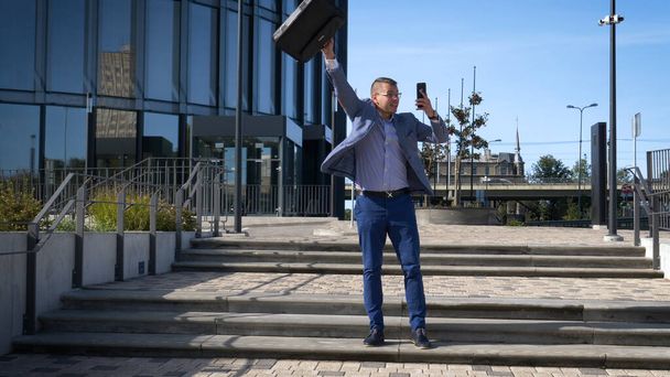 Celebrating success. Low angle view of excited young businessman keeping arms raised and expressing positivity while standing outdoors with office building in the background - Fotoğraf, Görsel