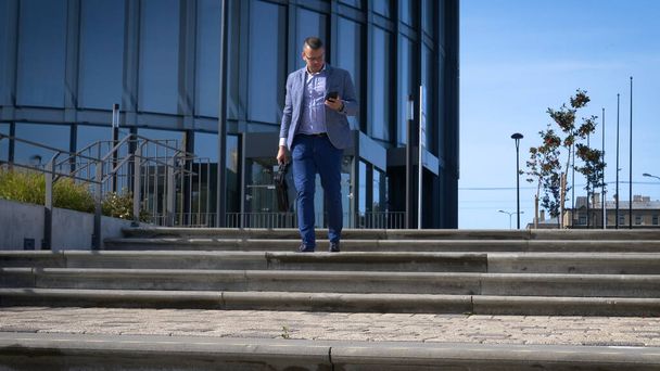 Celebrating success. Low angle view of excited young businessman keeping arms raised and expressing positivity while standing outdoors with office building in the background - Fotografie, Obrázek