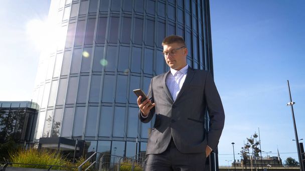Celebrating success. Low angle view of excited young businessman keeping arms raised and expressing positivity while standing outdoors with office building in the background - Zdjęcie, obraz