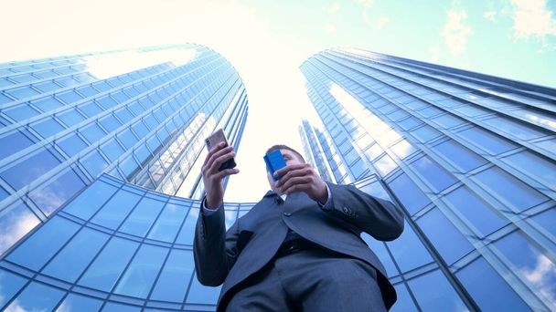 Business man using mobile phone for shopping online using credit card or internet. Concept of: Banking, Business, Skyscrapers of business centre at the background. - Фото, зображення