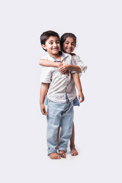 Cute little Indian asian siblings standing and embracing each other in white clothes while standing againstwhite background. - Foto, imagen