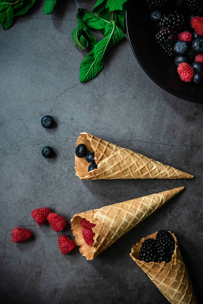 Top view of fresh berries and in waffle cones on dark stone background. Concept healthy food and desert. - Foto, Imagem