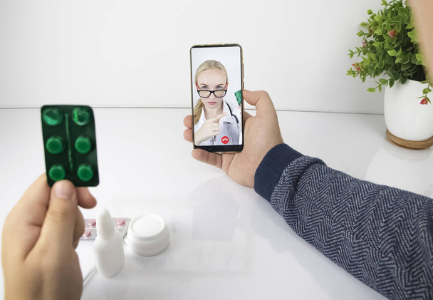 Egy férfi egy okostelefonon keresztül kommunikál egy orvossal videokapcsolaton keresztül. Orvosi segítség karantén alatt. Távoli konzultáció egy terapeutával - Fotó, kép