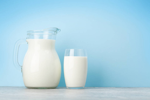 Молоко в стакане и кувшин перед синим фоном с копировальным местом - Фото, изображение