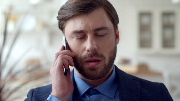 Серьезный бизнесмен говорит на мобильном телефоне в домашнем офисе. Парень говорит по телефону. - Фото, изображение