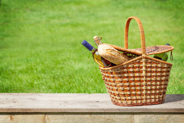 Piknik kosár borral és bagettel a kerti asztalon. Fénymásolási hellyel - Fotó, kép