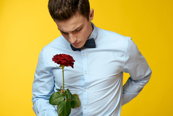 Elegáns férfi öltönyben, vörös rózsával a kezében, sárga háttérrel, kivágott kilátással. - Fotó, kép
