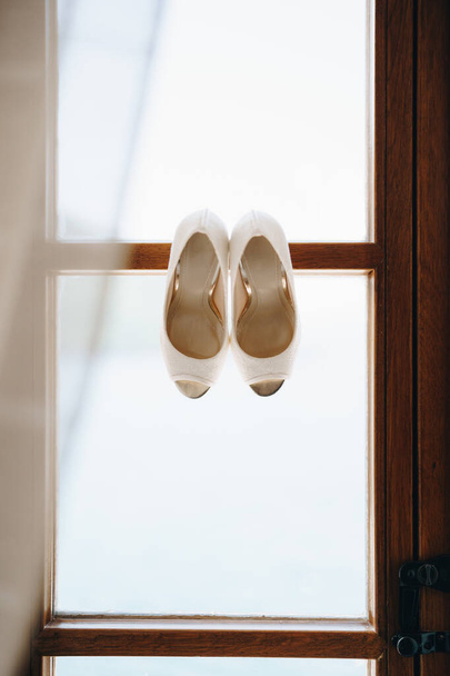 Chaussures mariées blanches sur un cadre de fenêtre en bois sur fond blanc. - Photo, image