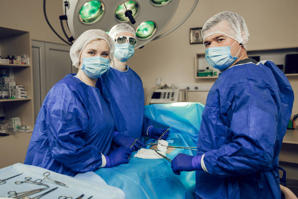 Portret trzech chirurgów w pracy. Lekarze przygotowują się do operacji. Chirurdzy i pacjent w szpitalu - Zdjęcie, obraz