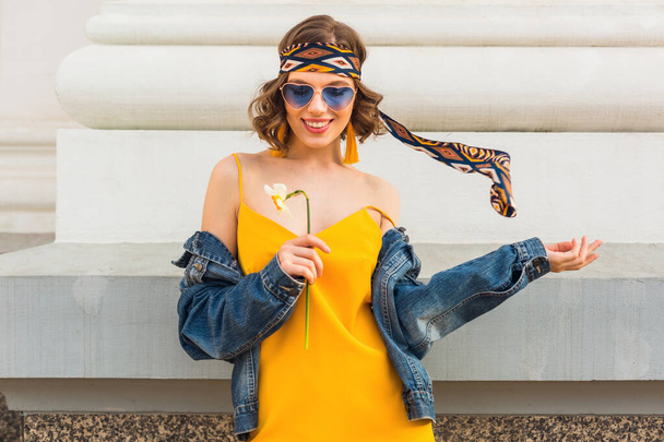 stylish attractive woman in hippie style outfit, yellow dress denim jacket, trendy accessories, sunglasses, smiling, happy positive mood, street fashion, spring summer fashion trend, cheerful emotion - Foto, afbeelding