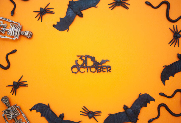 Halloween-Flatlay mit Schlangen, Luftschlangen und Spinnen und einem Skelett auf orangefarbenem Hintergrund, leere Textfläche, gruseliges Urlaubskonzept, herbstliche Horrorgeschichten. - Foto, Bild