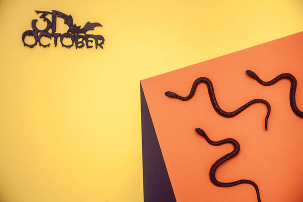 31 ottobre su sfondo arancione, posa piatta di serpenti su carta piegata geometricamente, concetto di Halloween. - Foto, immagini