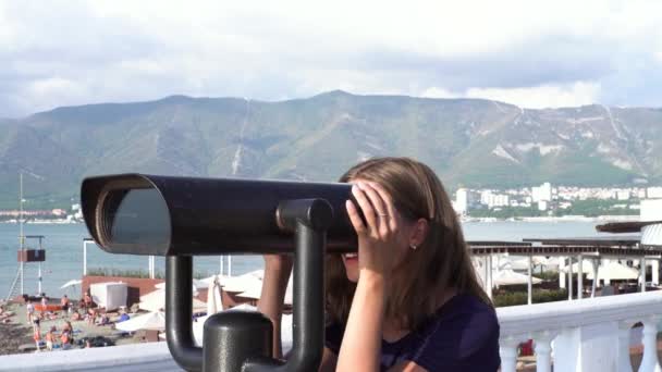 Fille heureuse profitant d'une vue marine grâce au binoscope. Les médias. Jeune femme utilise monnaie opéré binoculaire pour observer paysage, océan, plage, scènes à la côte. - Séquence, vidéo