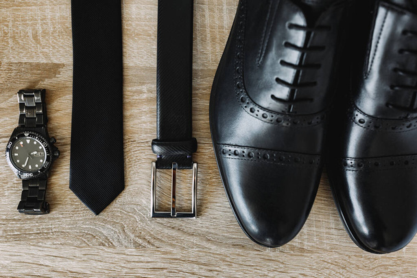 Nuevos zapatos para hombre, cinturón, corbata y reloj de pulsera en negro sobre una textura de madera. - Foto, Imagen
