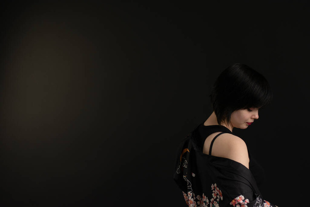 Κοντινό πορτραίτο. Όμορφο κορίτσι με μαύρο κοντό κούρεμα σε σκούρο φόντο στο στούντιο. Ασιατικό θέμα, Ευρωπαία με κιμονό. Φυσικό μακιγιάζ στέκεται με την πλάτη της. Spa, κουρείο - Φωτογραφία, εικόνα