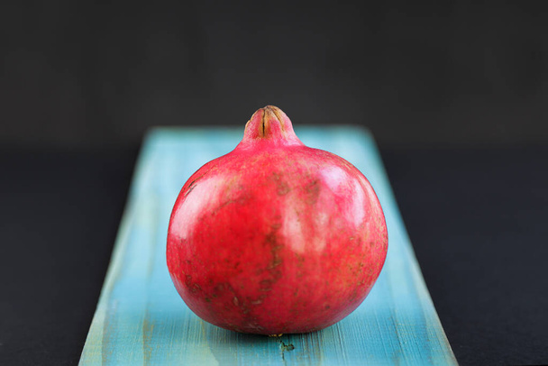Close up of a pomegranate fruit on cut board against black background - Foto, Imagen