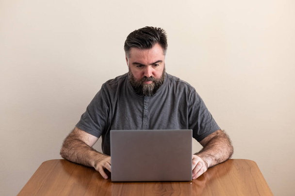 Белый белый мужчина с бородой, с ноутбуком, сидящим за столом. - Фото, изображение
