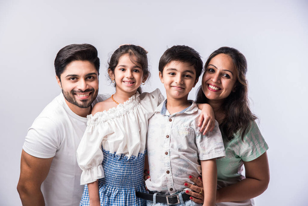Belle jeune famille indienne de quatre câlins, regardant à la caméra et souriant tout en se tenant debout sur fond blanc - Photo, image