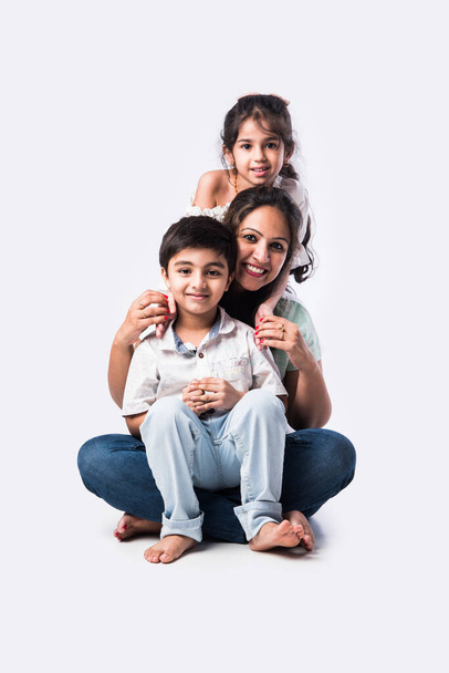 Portrait of Indian Asian young family of four sitting on white flour against white background, looking at camera - Photo, image