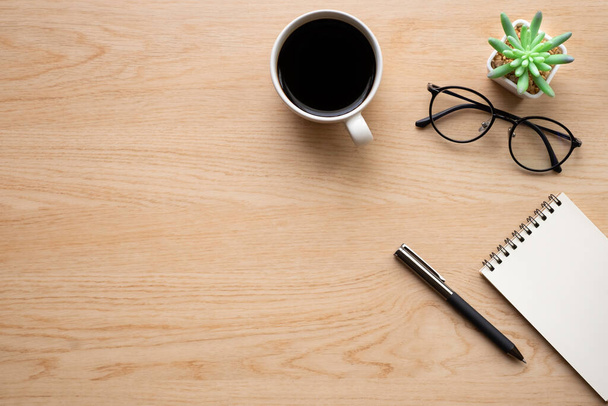 Top view above of Wooden office desk table with blank notebook, pen and coffee cup with glasses. Business and finance concept. Workplace, Flat lay with blank copy space. - 写真・画像