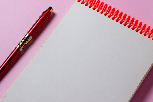 Σημειωματάριο και στυλό σε ροζ φόντο. Ένα καθαρό σημειωματάριο. Υπάρχει χώρος για μια επιγραφή ή λογότυπο στο σημειωματάριο - Φωτογραφία, εικόνα