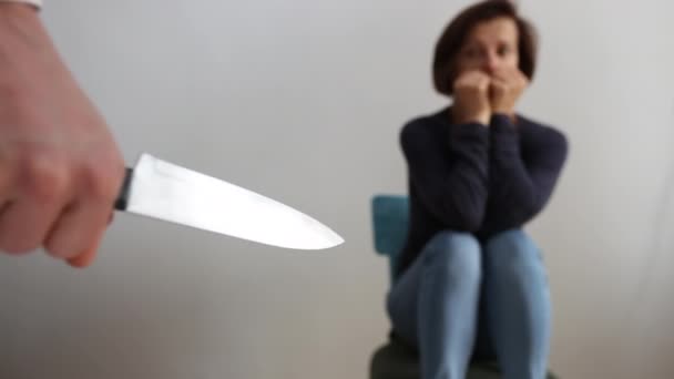 Κοντινό βίντεο με το χέρι του άντρα με μαχαίρι και γυναίκα να κάθονται στο βάθος τρομαγμένη. Έννοια της ενδοοικογενειακής βίας - Πλάνα, βίντεο