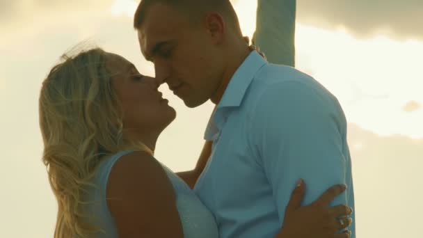 Két szerető sziluettje. Friss házasok naplementekor. A vőlegény megcsókolja a menyasszonyt, és gyengéden megöleli naplementekor. - Felvétel, videó