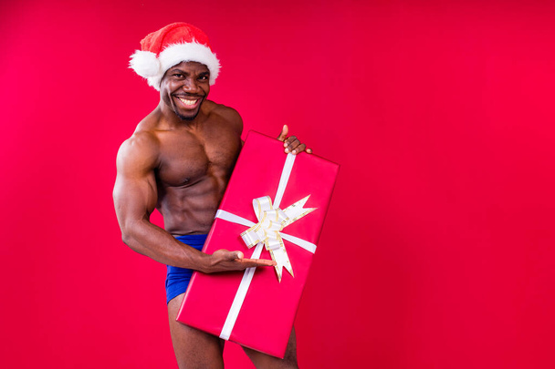 nude latino hispanic mixrd race man holding gift in studio red background - Photo, Image