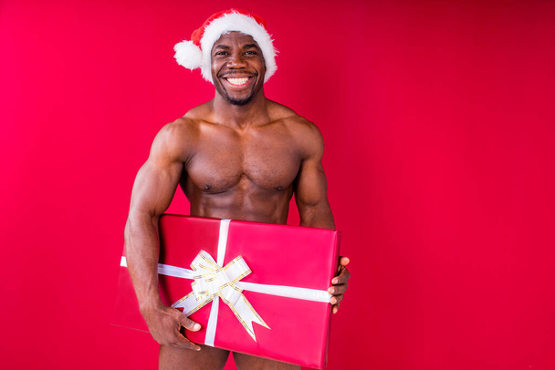 nude latino hispanic mixrd race man holding gift in studio red background - Photo, Image
