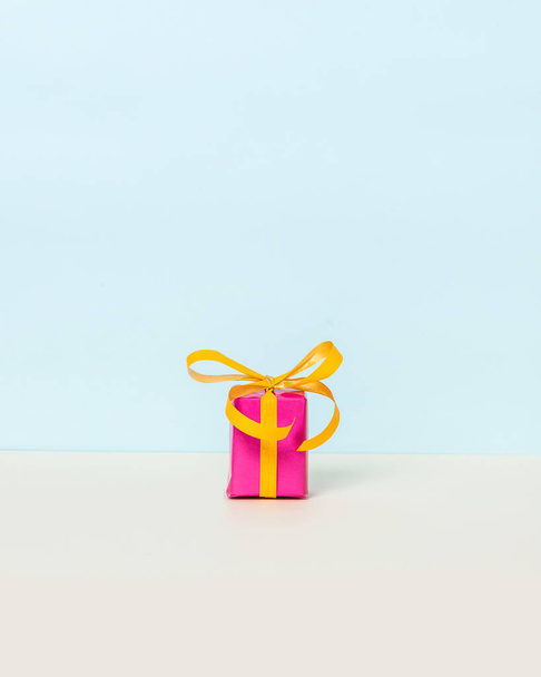 Magenta-Geschenkbox mit gelbem Band auf pastellfarbenem Hintergrund. Kopierraum. Frontansicht. - Foto, Bild